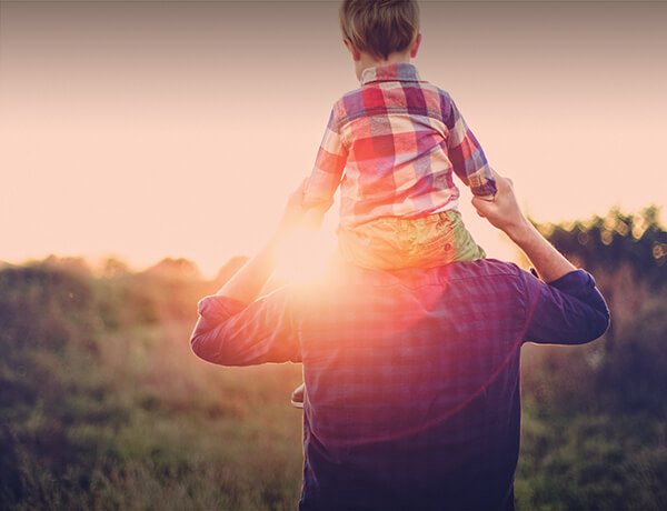 a dad with his son on his shoulders watching a sunset